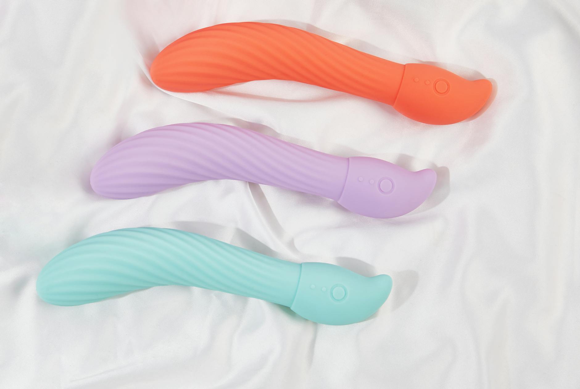 Three colorful vibrators arranged on white fabric showing smooth texture and design detail