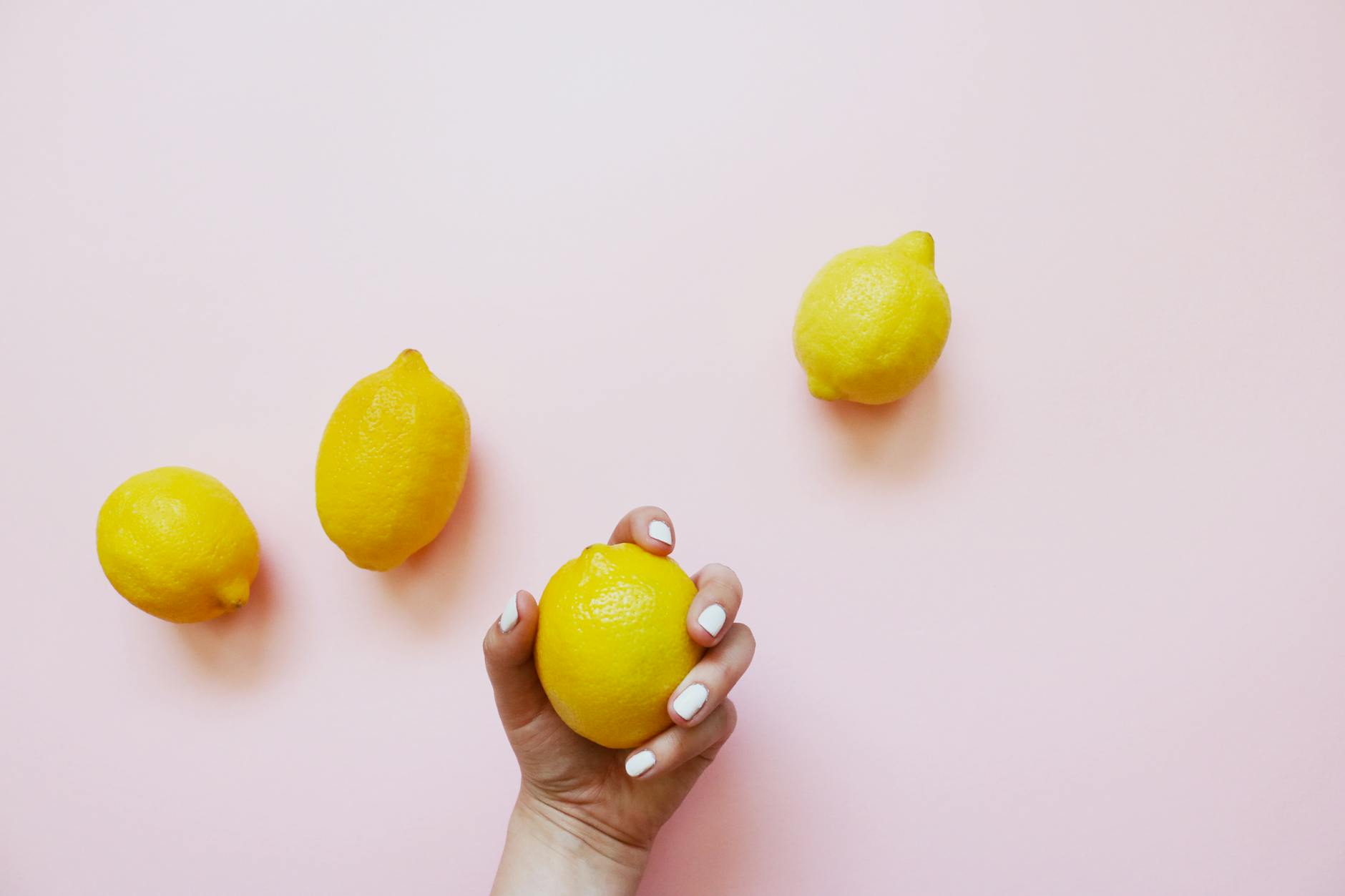 A hand holding a lemon on a soft pink background, representing gentle, non-abrasive pleasure