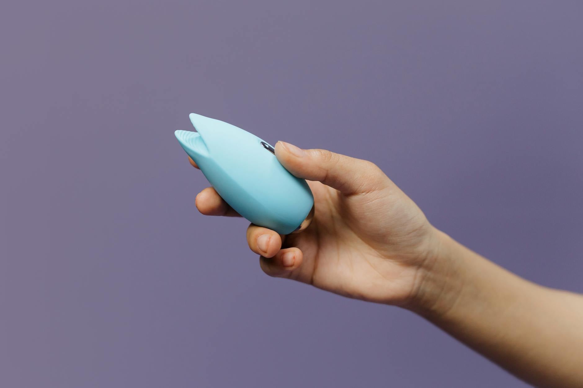 Un vibratore al limone blu in mano contro uno sfondo viola, promuovendo l'amor proprio e la sessualità.