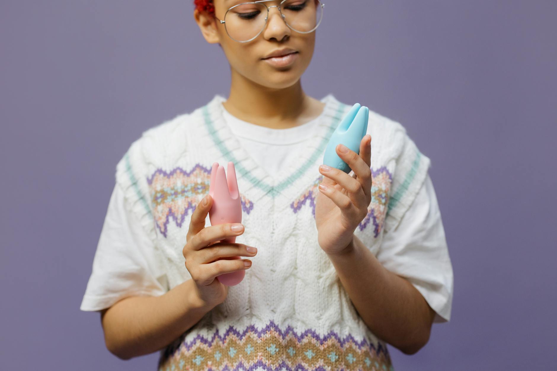Hand holding blue and pink silicone vibrators in a contemplative moment, representing pleasure recovery tools