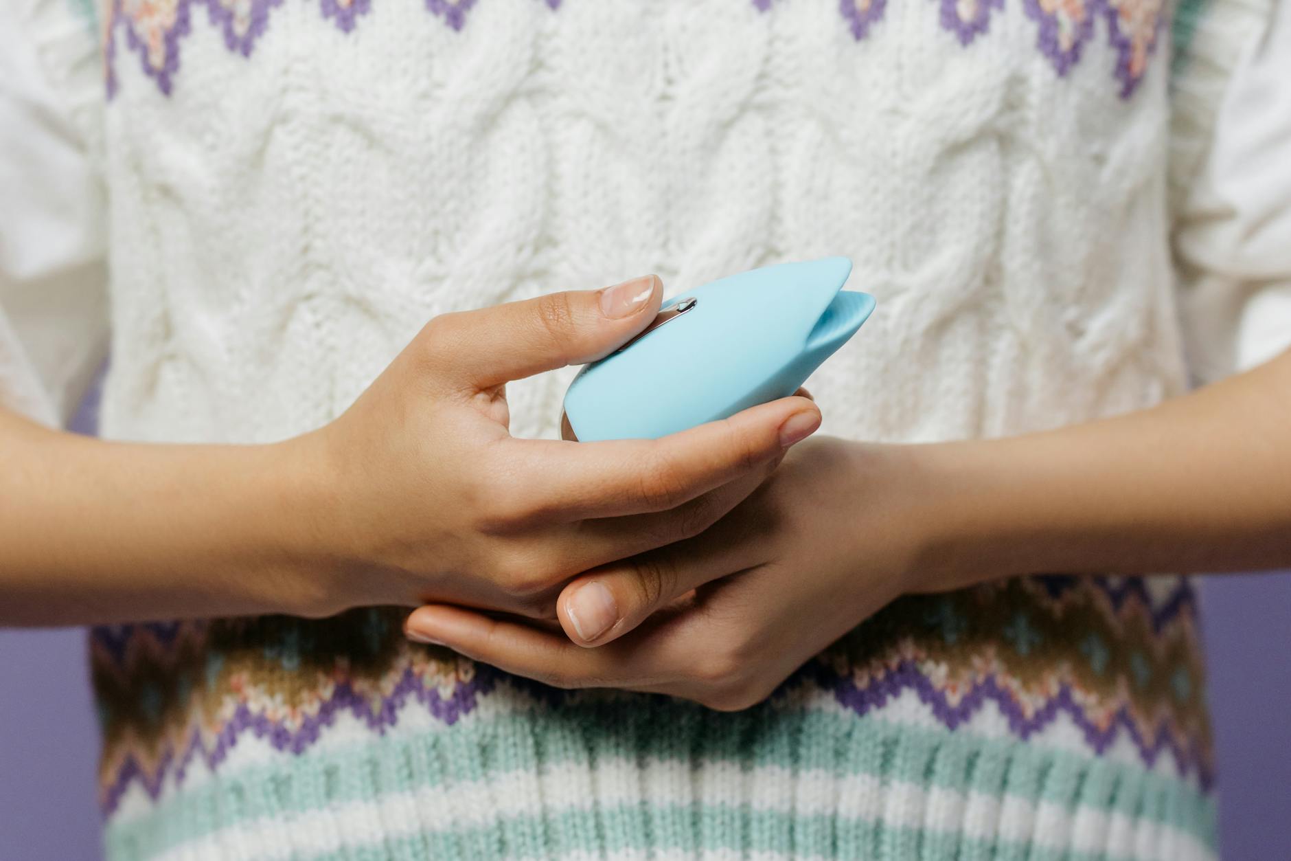 Un vibratore sessuale blu in silicone tenuto in mano contro uno sfondo viola solido, promuovendo l'amore verso se stessi e la sessualità.