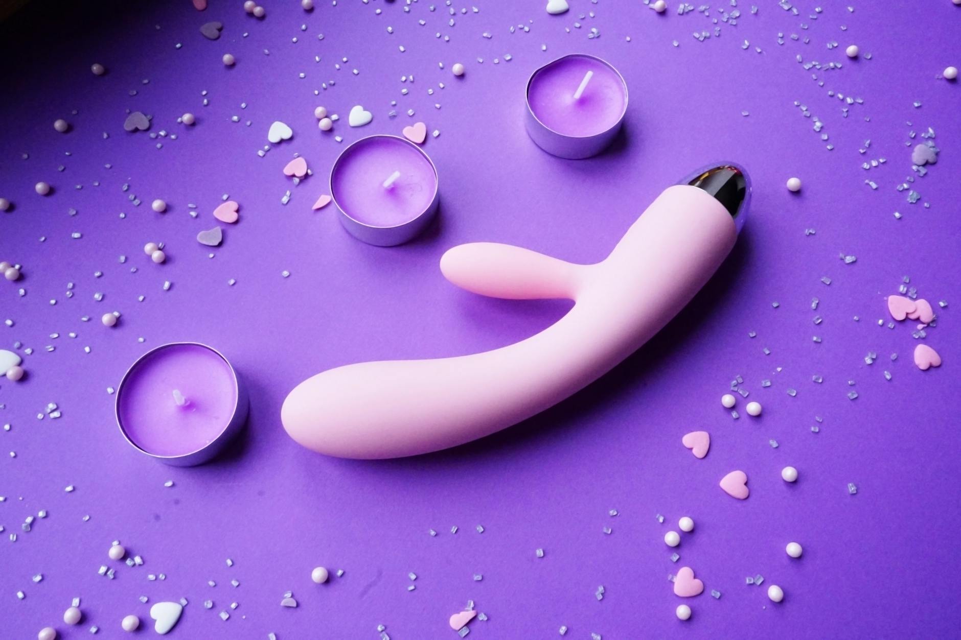 Pink lemon vibrator on a purple background with candles and confetti for intimacy